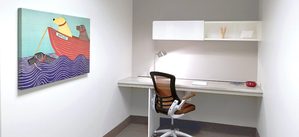 Minimalist office with a desk, chair, and wall-mounted shelves. A colorful painting of dogs in a boat hangs on the wall.